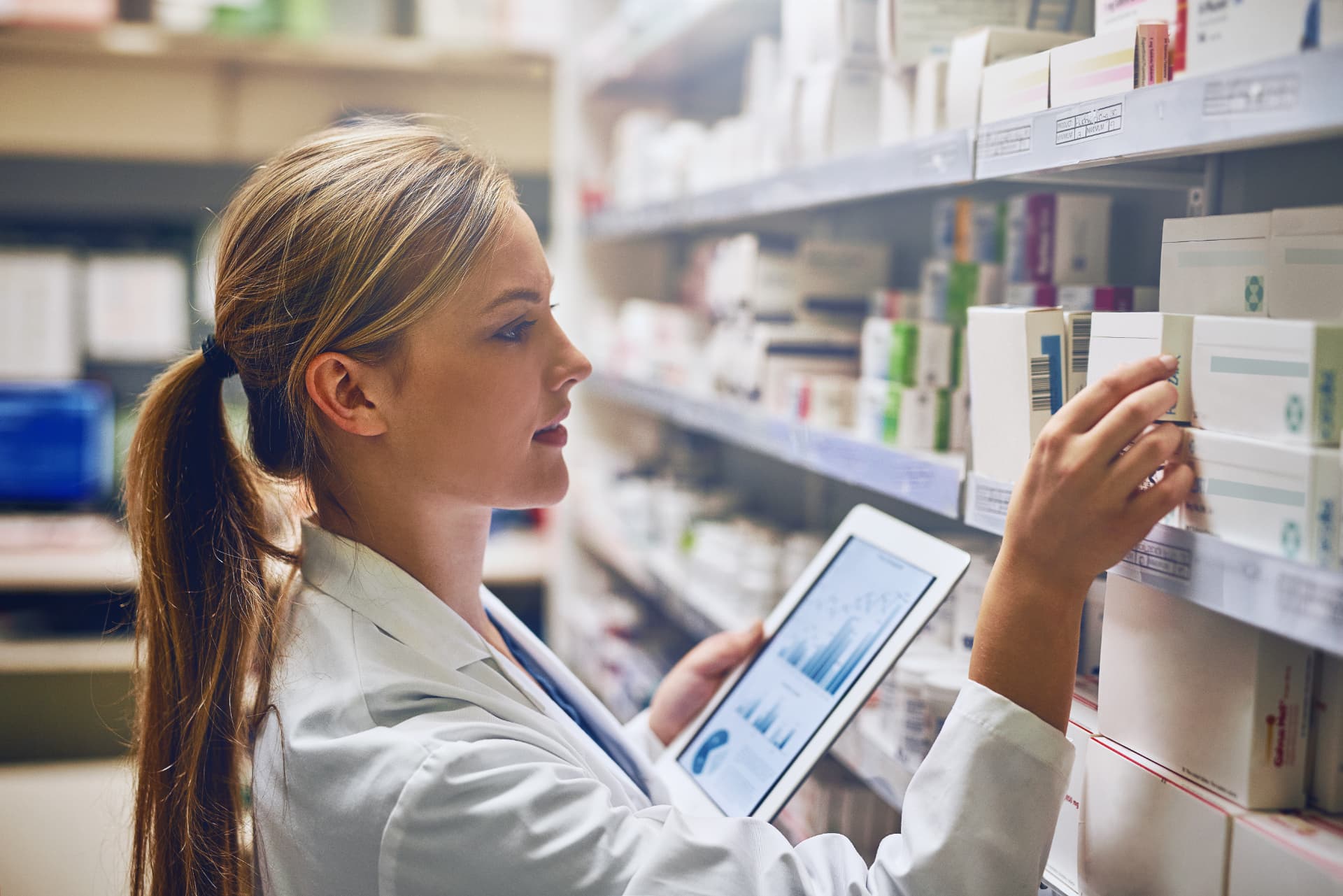 Apothekerin mit Tablet kontrolliert Arzneimittel im Regal